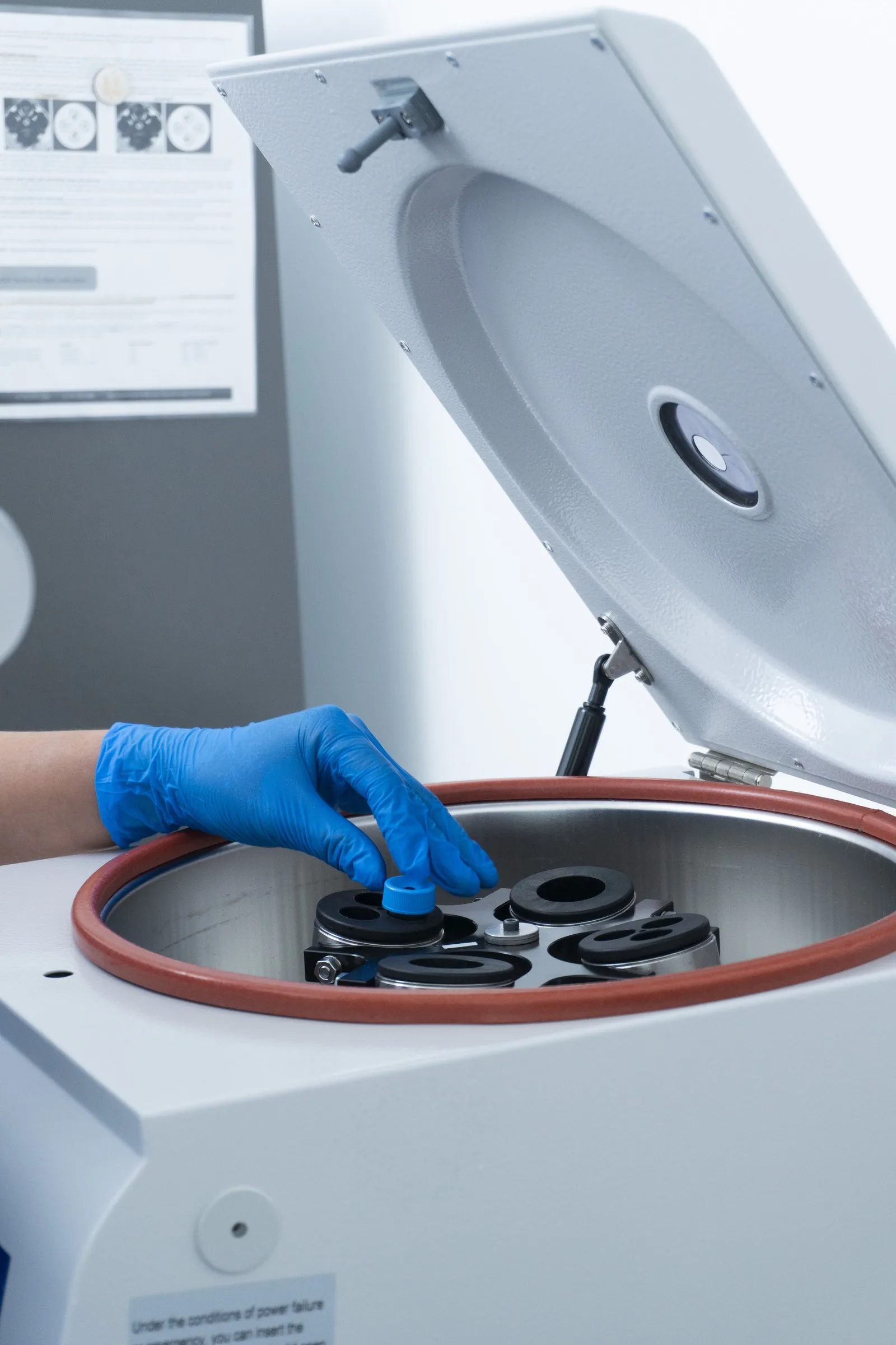 Gloved hand placing tubes into the open laboratory centrifuge.