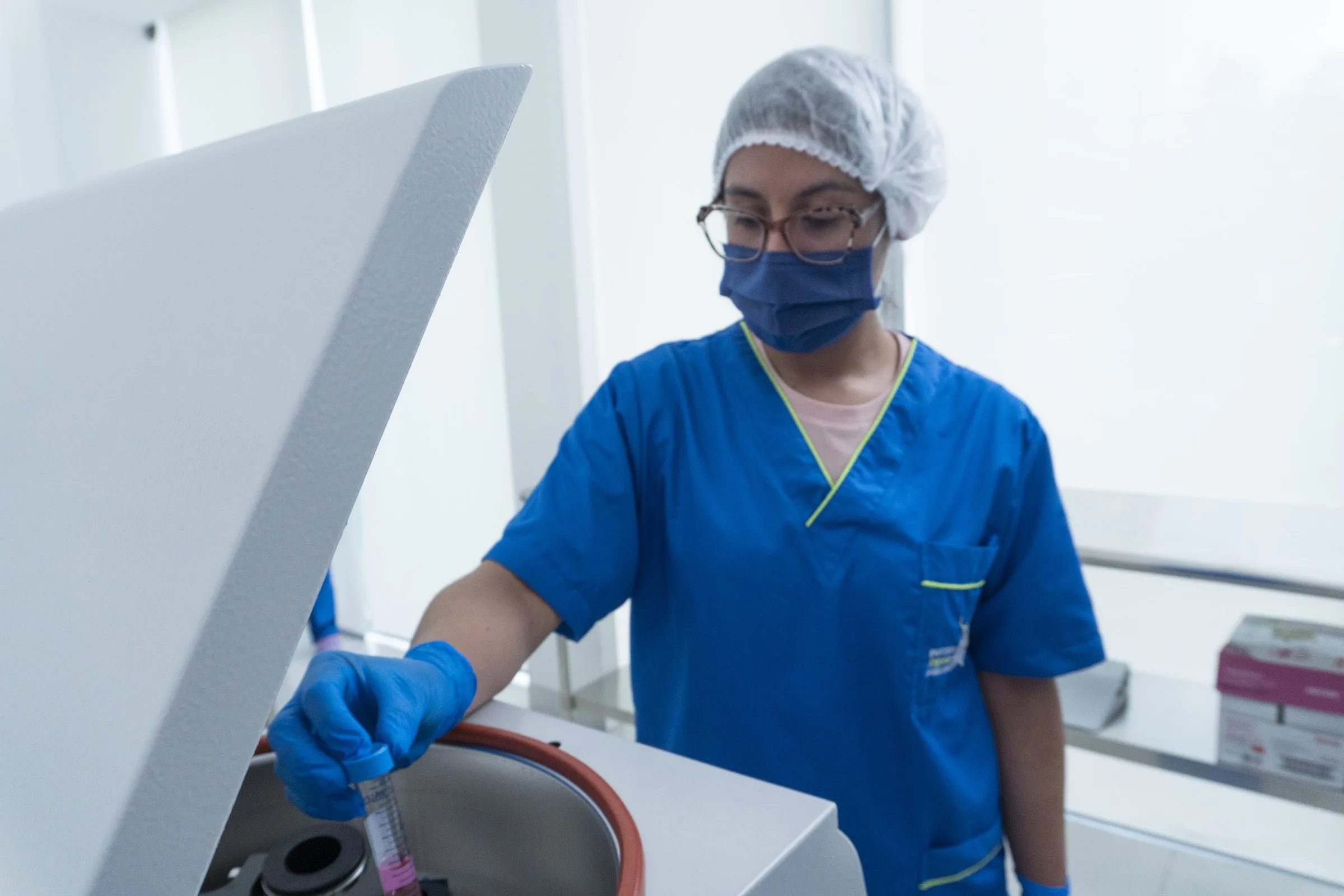 Laboratory technician in cap and mask placing a tube into the centrifuge.